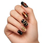 Faux ongles noirs et ambre à soleil, effet œil-de-chat et décors dorés portés sur une main — Darkin. @worn